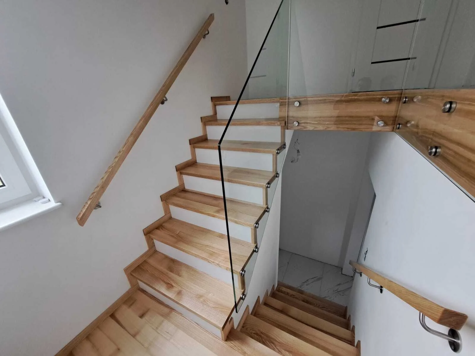 Detal szklanej balustrady samonośnej przy schodach jesionowych